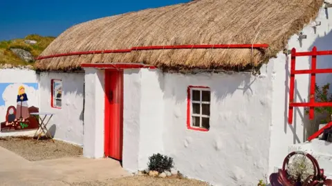 Getty Images A white thatched cottage with red doors and windows