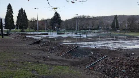 Railings of the sports court are flattened, and the tennis courts are almost swamp-like, covered in thick, dark silt at Pontypridd Lido