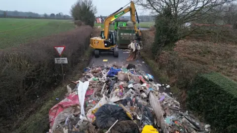 Contractors work to remove a pile of waste from Watery Lane, on the outskirts of Lichfield in Staffordshire.
