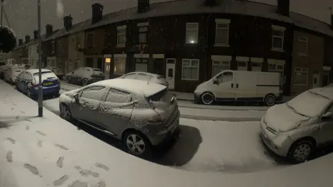 Snow on a street, with cars parked either side