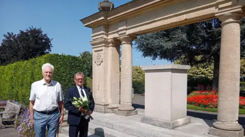 Guildford Borough Council Armed Forces Champion, Councillor Stephen Hives, with Graham Chilton, secretary of the Surrey Branch of Malaya and Borneo Veterans Association on 80th anniversary of VJ Day at Guildford Castle war memorial. Mr Hives is holding white lilies. 