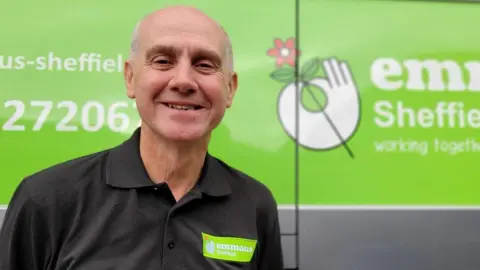 Carl Dray, a senior man, stood in front of a green Emmaus-branded van, wearing a similarly branded shirt.