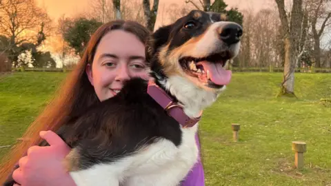 Jessica, with long brown hair, cuddles Zola, a black and white collie. Zola 