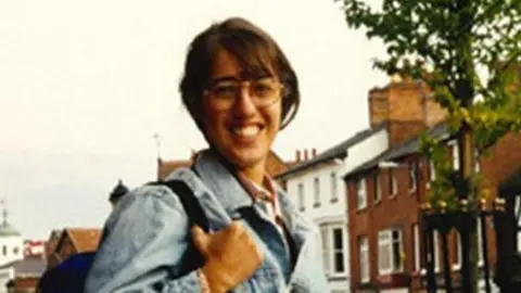 A young woman smiles wearing a denim jacket and glasses in a clearly old colour picture
