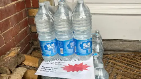 Julia Gregory/BBC A pile of bottles of water on a doorstep in Bramley