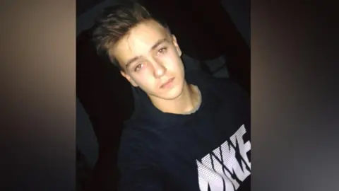 Devon and Cornwall Police A young man with brown hair and brown eyes is wearing a dark navy top with the word Nike in white on it. 