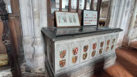The grey granite tomb of Thomas Chaucer and his wife Maud in St John Baptist's Chapel in Ewelme Church, St Mary the Virgin. The tomb is decorated with their coats of arms in colour, and those of royal and noble families they had connections with. 