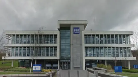 The headquarters of Durham Police is a three-storey white building mostly made of glass. It is surrounded by a small landscaped area. 