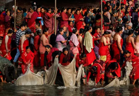 Navesh Chitrakar/Reuters Women dressed in red wash clothes in a river