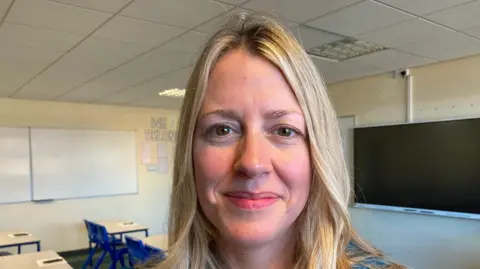 BBC/Amy Garcia Gillian is a middle aged woman with shoulder length blond hair and brown eyes. She wears a teal blue suit jacket and black top underneath. 