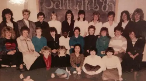 University Hospitals Bristol and Weston An old photograph of 25 women as they began their nurse training together in 1985. They are in an arch made up of three rows and are all smiling at the camera. There is a board in the background with January '85 written on it.