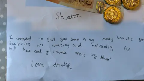 Contributed A letter written by a girl that reads: "Sharon, I wanted to give you some of my money because your sculptures are amazing and hopefully this will help and go towards more of them! Love Amelie." There are some pound coins and a £10 note resting at the top of the letter.