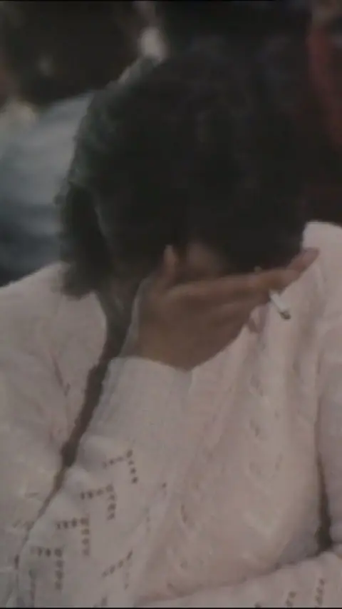 Woman in a white jumper with her head in her hand which is also holding a cigarette