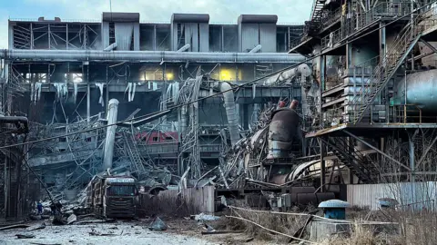  Ground of the factory littered with debris, including collapsed ceilings and pipes. 
