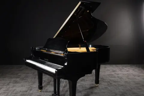 Propstore A black Yamaha grand piano standing in a dark room with grey carpet and black walls.