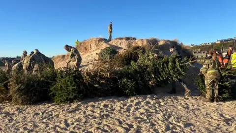 BBC People in camouflage with Christmas trees on a beach