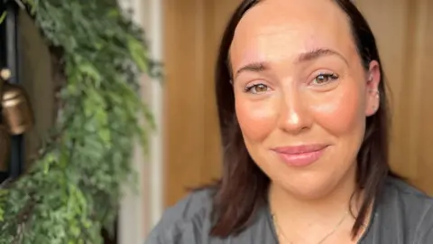 A woman with brown hair is smiling into the camera