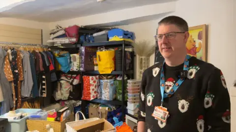 Chris Smith, employment buddy at Space4Autism. He is standing in the charity's donations room, with clothes and bags of other items behind him.