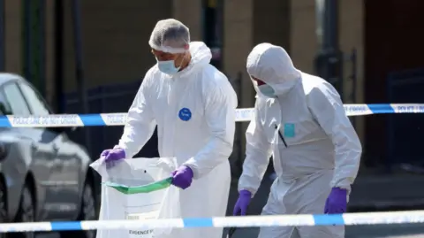 Reuters Two forensic officers in white overalls between police tape
