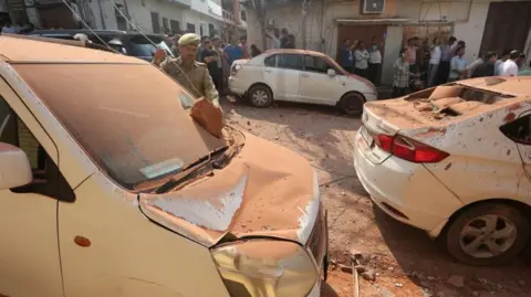 People gather around damaged vehicles and houses after shelling, at Jammu town in Indian-administered Kashmir on 10 May 2025