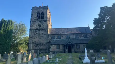 Photograph of St Wilfred's Church in Mobberley, Cheshire. The image shows a church and headstones in the graveyard.