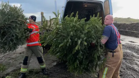 Two men carrying a large Christmas tree out of the back of a van