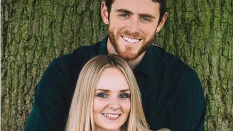 PA Media Police officer Andrew Harper, off duty, clasps his hands around his wife, Lissie, who puts her hands over his. They are both facing the camera, smiling. 