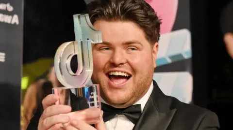Morgan James holding a glass award which is in the shape of the TikTok logo.