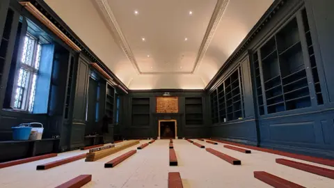 National Trust Image of Avebury Manor West Library interior with wooden planks on the floor, ready for renovation, and dark blue book cases around the edge of the room. 