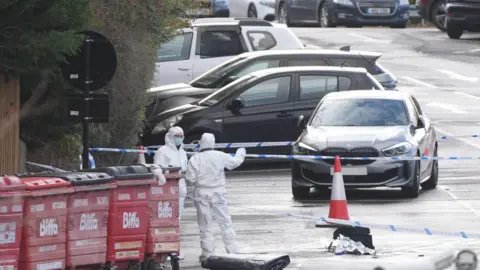 PA Media Police cordon off area around Dave Scott's car. It is a grey BMW surrounded by police tape, with two forensics officers stood next to bins in the foreground.