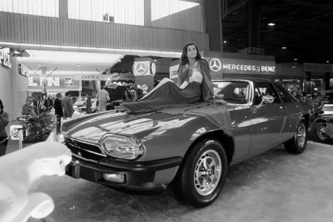 Getty Images A black and white image of a Jaguar XJS at a car show with a model sitting on the bonnet