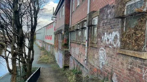 Sheffield Council Derelict and vandalised buildings overlook a scrubby path by a canal