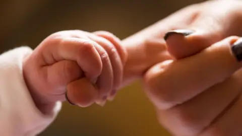 A newborn baby's hand holds on to mother's index finger