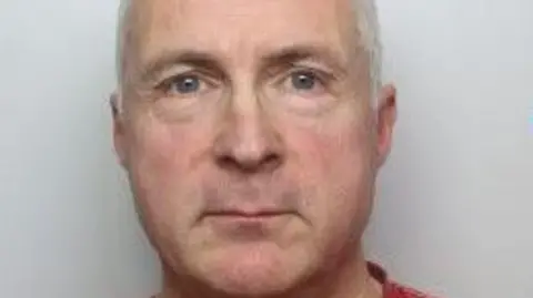 Philip Maylen has a neutral expression in a police custody image. He has short, white hair and is clean-shaven