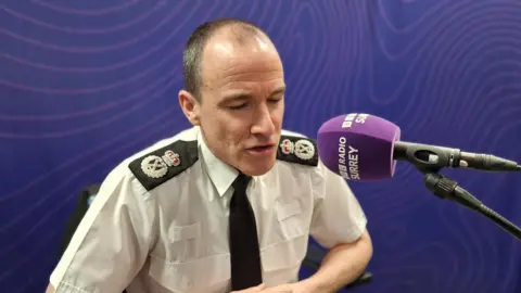 A man in a white shirt and black tie speaking into a purple microphone