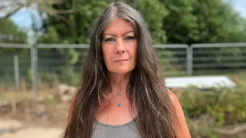 Annette Holliday looking at the camera wearing a grey top with long brown hair.