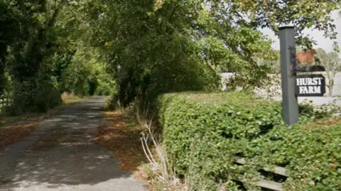 A track with trees either side and a sign which reads Hurst Farm