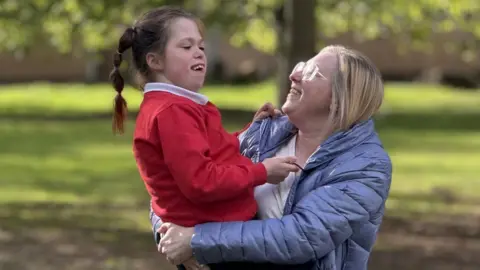 Vanellope is being held in the arms of her mum Naomi as they walk in the park