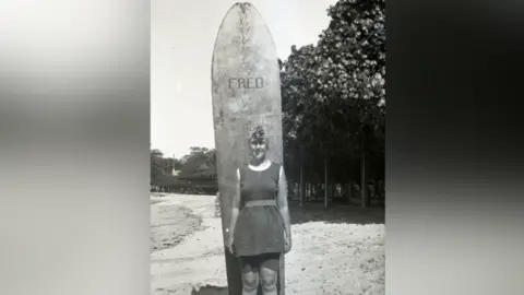 Christie Archive Trust Agatha Christie with surfboard on Waikiki Beach in Honolulu in 1922. She is smiling.