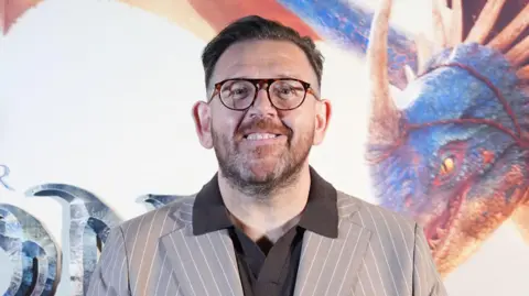 PA Media Nick Frost wearing a brown suit and brown-framed glasses.