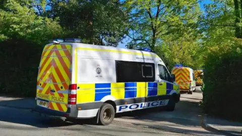 Three police vans in a row, parked in a a small side road. There are trees either side of the road.