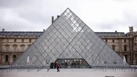 EPA The outside of the glass pyramid at the Louvre Museum in Paris on a grey day, with personnel outside, one of whom is wearing a high-vis jacket
