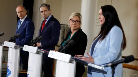 Reuters From left to right, Micheál Martin, Simon Harris, Michelle O'Neill and Emma Little-Pengelly stand behind podiums. 