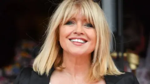 Getty Images A woman with shoulder length blonde hair and a fringe. She is smiling and wears a black blazer. 