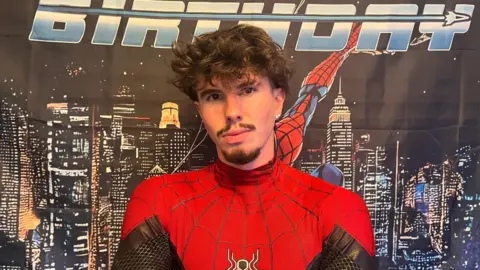 A young man in a red and black superhero costume. 