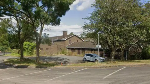 A view of a boarded up building with visible shrubbery growing on the edges of the walls.