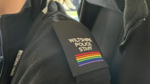 Call operator's epaulette that reads "Wiltshire Police Staff" with rainbow bars underneath the text