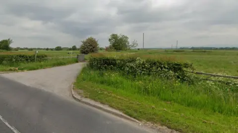 The entrance to the farm can be seen, with trees in the distance.
