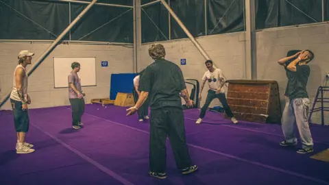 Lisa Beebe A group of young men stand in a gym studio in jeans T shirt and trainers