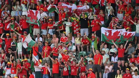 A crowd of Wales fans, some of which are holding up a Welsh flag